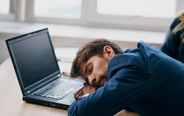 Egy öltönyös férfi egy munkaasztalnál egy laptop iroda előtt fáradt. - Fotó, kép