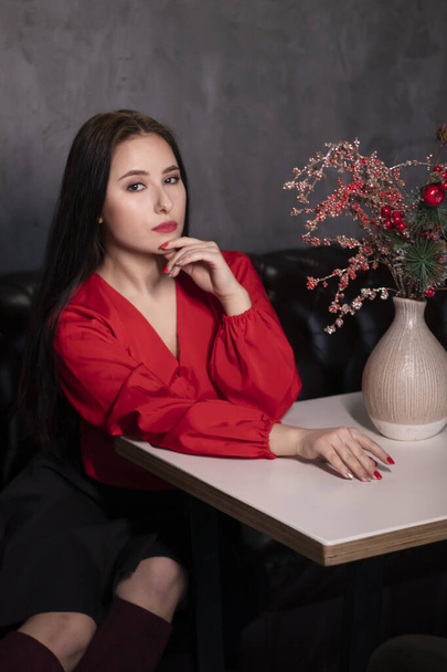sexy mujer morena atractiva en blusa roja y falda negra en una cafetería vintage loft cerca de un jarrón con ramas rojas brillantes decorativas. espacio de copia. San Valentín  - Foto, imagen