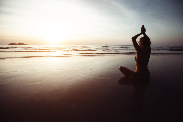 Yoga σιλουέτα της γυναίκας σε Lotus θέτουν στο ηλιοβασίλεμα παραλία της θάλασσας. - Φωτογραφία, εικόνα