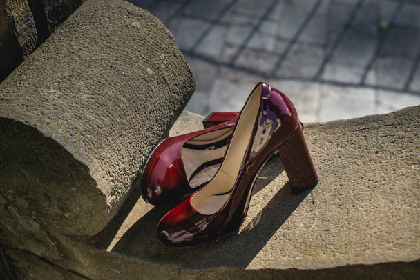 Bőr cseresznyés nők cipője a kőfalon. divat koncepció, női cipők, kiegészítők. burgundia lakkozott bőr cipők - Fotó, kép