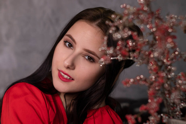 retrato de atractiva mujer morena en blusa roja cerca de decorativo boquet ramas rojas brillantes. espacio de copia. San Valentín  - Foto, Imagen