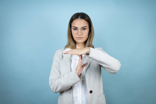 Young business woman over isolated blue background Doing time out gesture with hands, frustrated and serious face - Photo, Image
