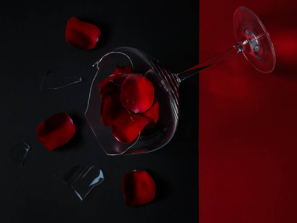 verre cassé et pétales de rose reposent en diagonale sur un fond rouge et noir, vue rapprochée sur le dessus. - Photo, image