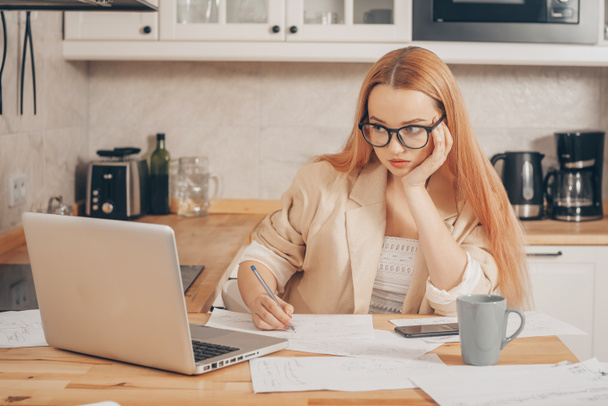 Woman at laptop works from home, student, teacher. A beautiful blonde in a jacket and glasses looks into a laptop and writes something down. Online training, work freelance accountant. - Valokuva, kuva