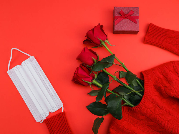 Roses, sweater, gift and mask lie on the right on a red background, close-up top view. - Fotografie, Obrázek