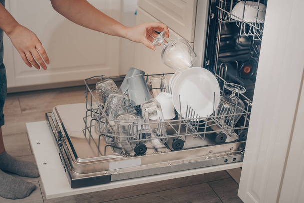 Built-in dishwasher, dishwashing. A woman loads washed dishes, cups, glasses. A woman's tender hand puts a glass goblet in the dishwasher or pulls out, unloads. - Fotoğraf, Görsel