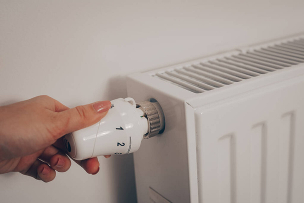 Το χέρι μιας γυναίκας γυρίζει το κουμπί θέρμανσης μπαταρίας. Θέρμανση σε ένα διαμέρισμα, στο σπίτι. Τιμές θέρμανσης. - Φωτογραφία, εικόνα