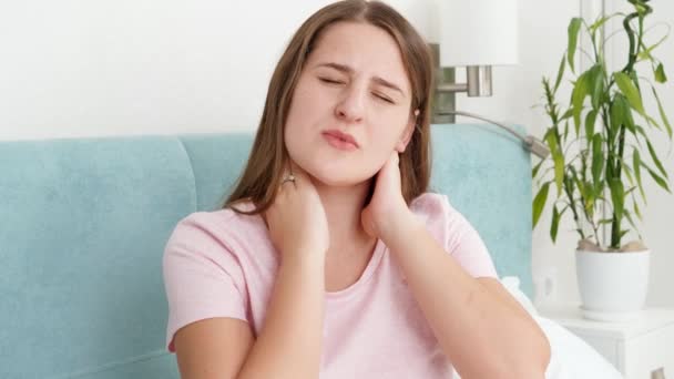 Jonge vrouw in pyjama die last heeft van pijn in de nek en rug na het slapen op een ongemakkelijk bed of kussen. - Video