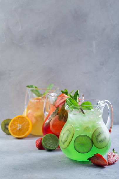 Different color lemonade in glass decanters with fruits and garnished with fresh mint and sliced fruits - 写真・画像