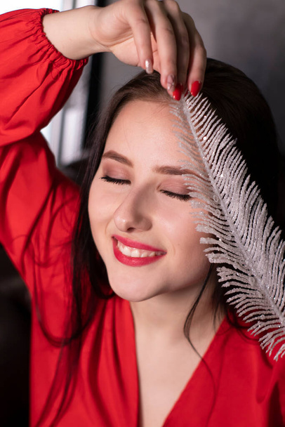 portrait of attractive brunette woman in red blouse with a big white feather. st valentines day, romance, romantic. copy space. - Zdjęcie, obraz