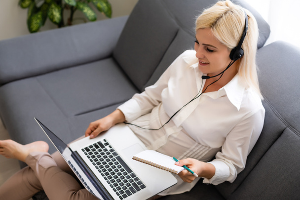 Beautiful smiling female student using online education service. Young woman looking in laptop display watching training course and listening it with headphones. Modern study technology concept - Photo, image