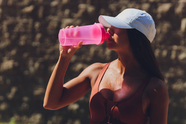 Toned belly and slim shape of athletic woman, holding a bottle of water and wearing a wristband. Morning running session in the city. spills on herself - Fotó, kép