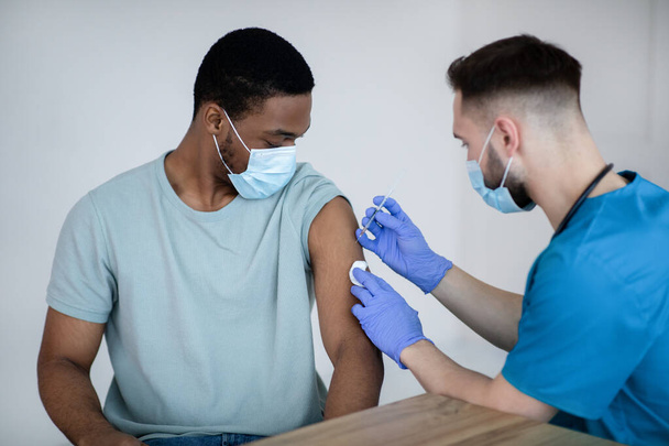 Paciente varón afroamericano vacunado contra covid-19, que recibe la vacuna antiviral inyectable en el centro de salud - Foto, imagen