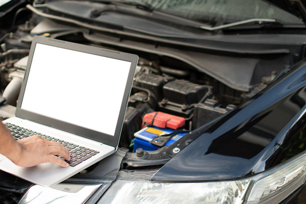 Close-up, een man de hand typen op een laptop computer toetsenbord om de werking van de motor van de auto in de garage te controleren. De motor van een auto start niet. Een notebookcomputer is een wit scherm en een blanco - Foto, afbeelding