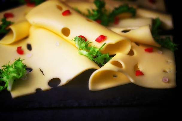 Slices of hard maasdam cheese on a dark background. Cheese with holes. - Photo, Image