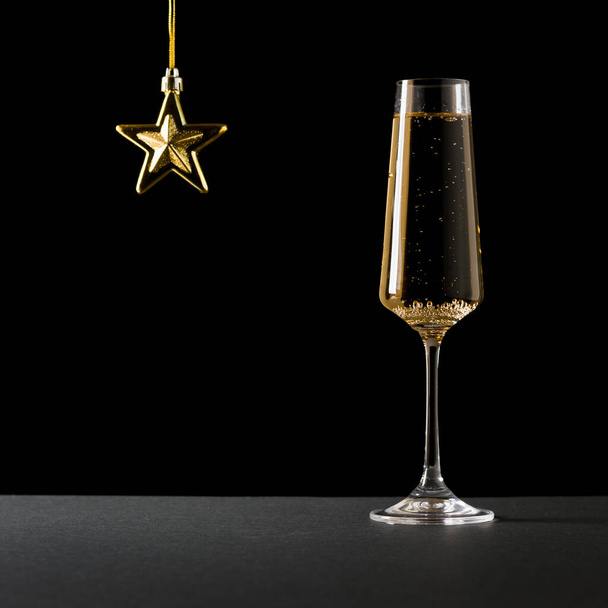 背の高いガラスのスパークリングワインと黒の背景の金の星。人気のアルコール飲料. - 写真・画像
