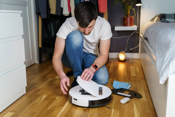 Robot vacuum cleaner repair. Man fixing robot vacuum cleaner DIY at home on the floor. Robotic vacuum cleaner maintenance and service. Smart device for easy housework. New tech for households. - Fotó, kép