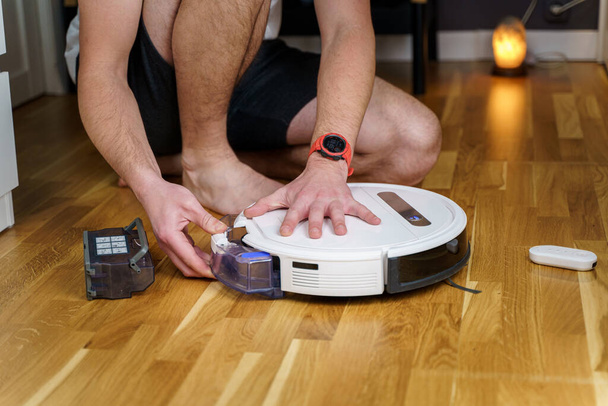 Robot vacuum cleaner repair. Man fixing robot vacuum cleaner DIY at home on the floor. Robotic vacuum cleaner maintenance and service. Smart device for easy housework. New tech for households. - Photo, Image