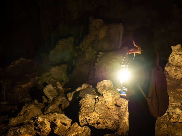 Elinde bir gaz lambasıyla gezen kaşif kadın çok karanlık ve doğal dikitlerin ve kayalık mağaraların içinden geçmek için parlak ışıklar kullanıyor.. - Fotoğraf, Görsel