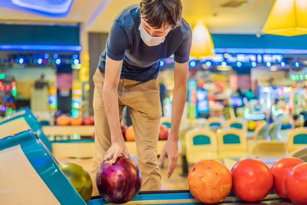 Man playing bowling with medical masks during COVID-19 coronavirus in bowling club - 写真・画像