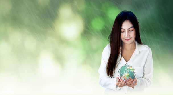 Weltumwelttag-Konzept: Asiatische Frauenhände halten Erdkugel vor verschwommenem grünen Wald mit Regenhintergrund. Elemente dieses von der NASA bereitgestellten Bildes - Foto, Bild