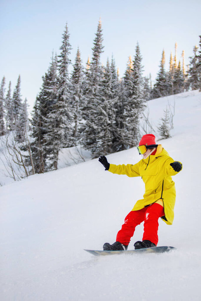 Femme est snowboard sur la pente d'une montagne enneigée dans une station naturelle. Matériel de ski : pantalon rouge et chapeau tricoté, veste jaune chaud, lunettes. Concentration sélective. - Photo, image