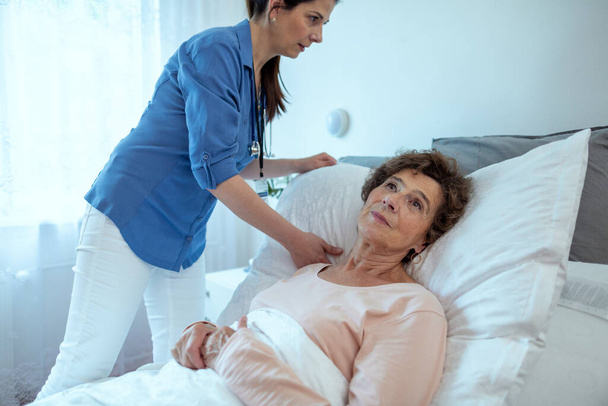Home Caregiver Adjusting Pillow For Elderly Female Patient. Nurse Taking Care of Senior Patient Lying in Hospital Bed.  - Photo, Image