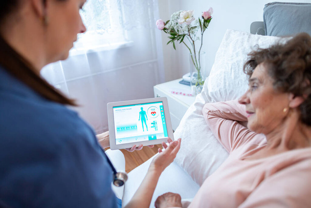 Доктор і старший пацієнт проходять через медичні результати на цифровому планшеті. Зосередьтеся на екрані цифрових планшетів, які показують записи здоров'я, які лікар пояснює літній жінці, що лежить у лікарняному ліжку
. - Фото, зображення