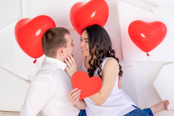 Valentinstag, ein Kerl mit einem schönen Mädchen schaut einander mit einem liebevollen Blick an, der ein großes rotes Herz in sich trägt - Foto, Bild