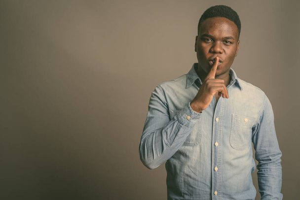 Jonge Afrikaanse man met vinger op lippen tegen grijze achtergrond - Foto, afbeelding