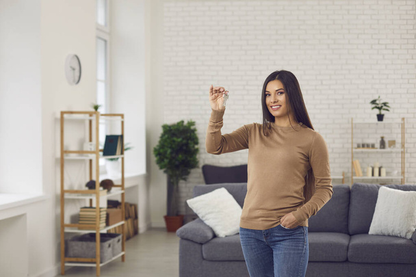 Happy single young woman standing in her new beautiful apartment and showing keys - Photo, Image
