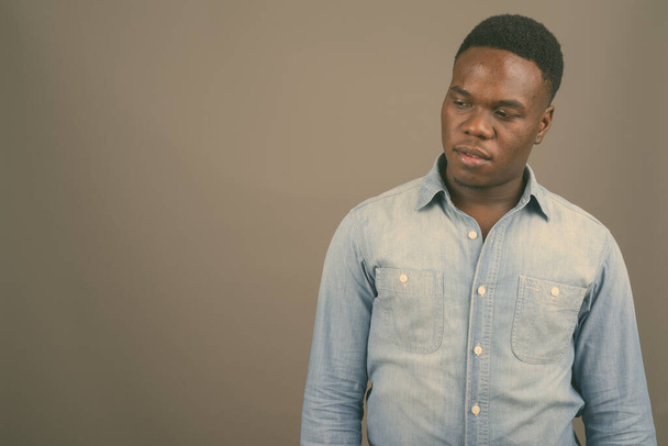 Young African man wearing denim shirt against gray background - Valokuva, kuva