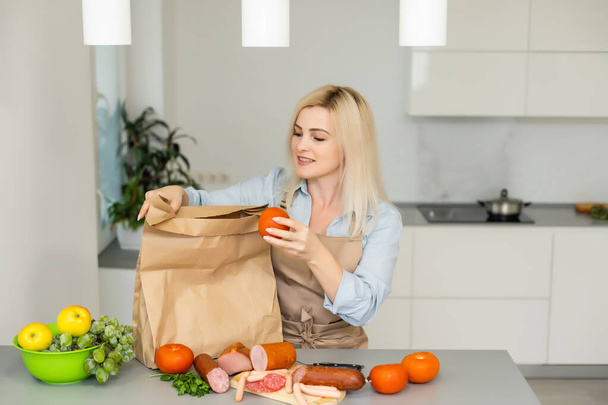 Conceito de Auto-isolamento. mulher desembalando saco de papel com alimentos na cozinha, pronto para quarentena durante surto epidêmico - Foto, Imagem