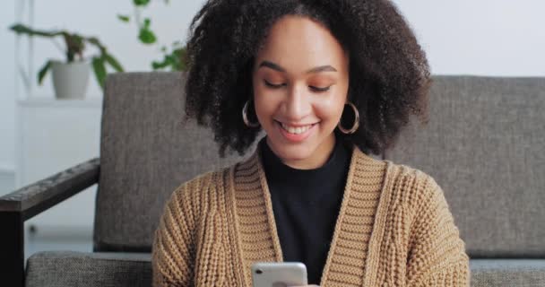 Portrét usmívající se afro americká žena při pohledu na telefon s úsměvem, dospívající dívka komunikující s přítelem nebo přáteli na sociálních sítích on-line při pohledu na kameru s uspokojeným ženským výrazem - Záběry, video