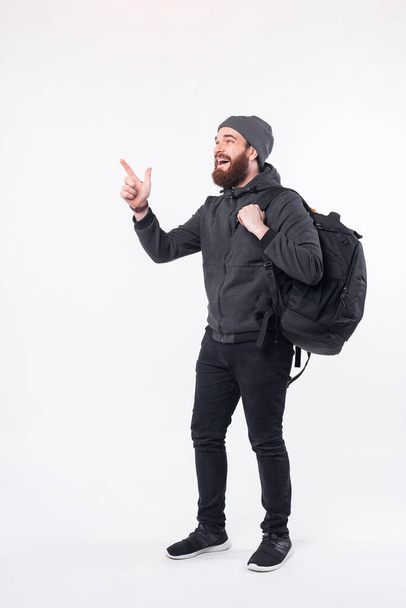 Photo of bearded hipster man wearing backpack and pointing away at the corner - Foto, imagen