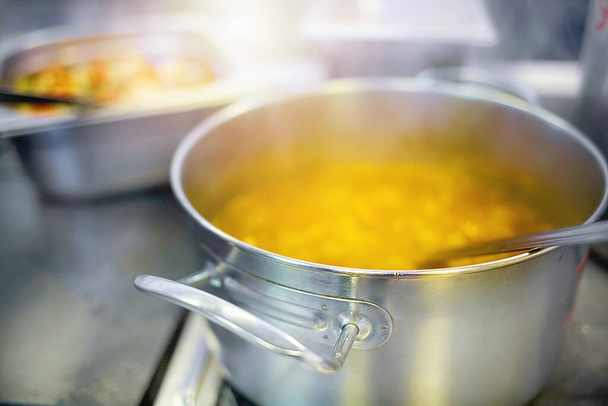 Przygotowanie pierwszego dania w jadalni. Zupa lub zupa jest gotowana w aluminiowym garnku na kuchence elektrycznej. - Zdjęcie, obraz