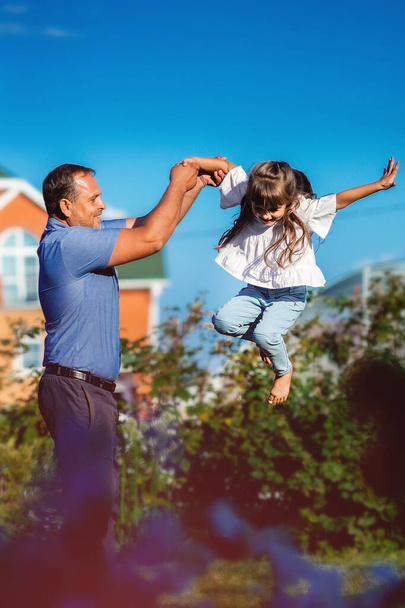 Onnellinen tyttö isänsä kanssa iloitsee kesäpäivänä luonnossa. Pieni lapsi hyppää korkealle isänsä avulla.. - Valokuva, kuva