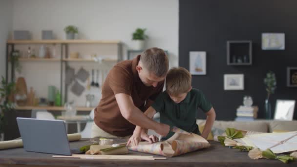 Střední pomalý záběr otce a syna, jak spolu tráví čas při ruční výrobě a doma dělají papírového draka - Záběry, video