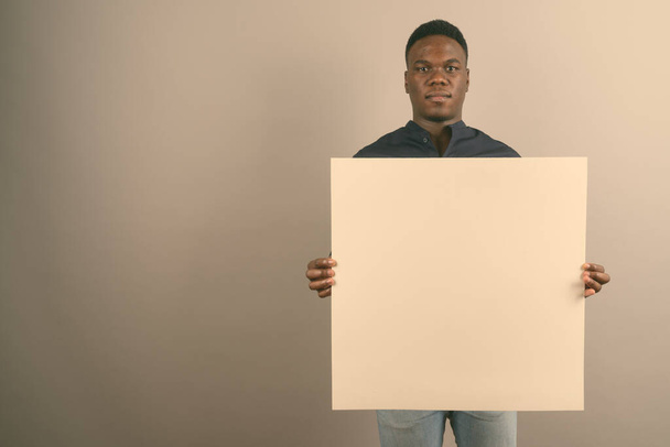 Young African businessman holding white board against white background - Fotó, kép