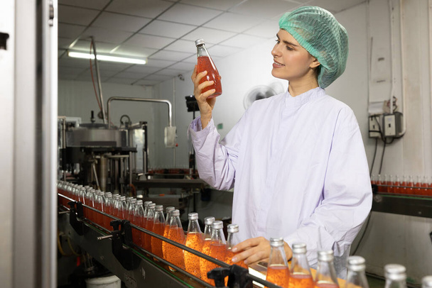 junge Fabrikarbeiterin sucht Basilikumsaatgetränk zur Qualitätskontrolle in Getränkefabrik - Foto, Bild