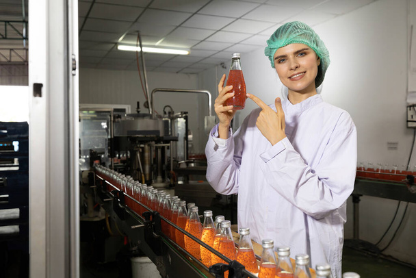 joven trabajadora de la fábrica mostrando y señalando la bebida de semilla de albahaca en la fábrica de bebidas - Foto, imagen