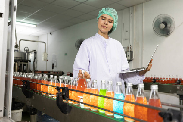 joven trabajadora de la fábrica recoger la bebida de semilla de albahaca para comprobar la calidad en la fábrica de bebidas - Foto, Imagen