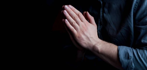 Hands in prayer. The man is praying. On a dark background. Hands out of the dark. - Photo, Image