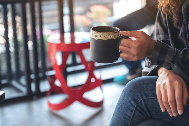 Крупним планом зображення жінки, що тримає і п'є гарячу каву, сидячи в кафе
 - Фото, зображення