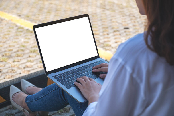 Makieta kobiety używającej i piszącej na laptopie z białym ekranem, siedzącej na parkingu na zewnątrz - Zdjęcie, obraz