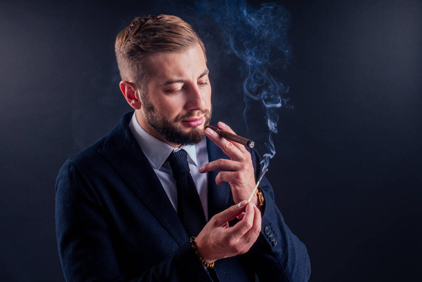 Portrait of an attractive business man with a cigar in black background studio - Foto, Imagem