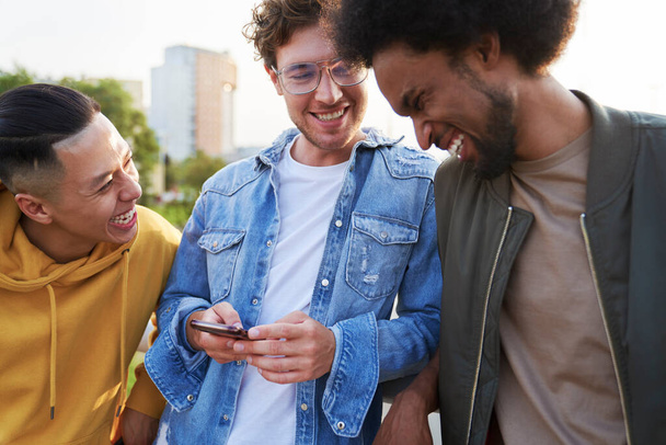 Tres jóvenes se ríen de algo que sostiene el teléfono móvil                                - Foto, Imagen
