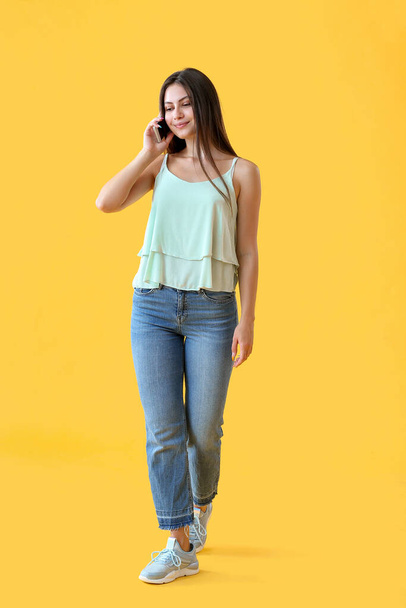 Beautiful young woman talking by mobile phone on color background - Фото, изображение