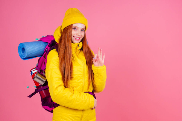 Happy woman ready to hiking in unknown place she is carries big backpack on shoulders in pink studio background - Foto, Bild