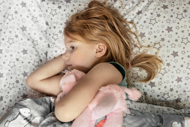 A little girl lies under a blanket with a toy dog getting ready for bed. - Photo, Image